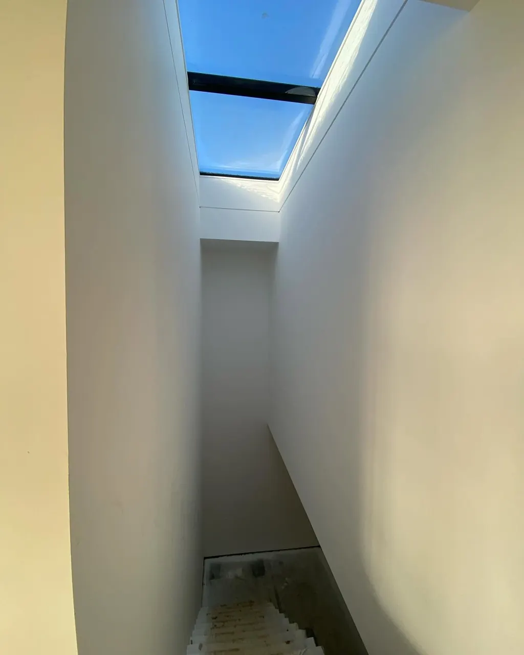 Narrow staircase painted white under a skylight