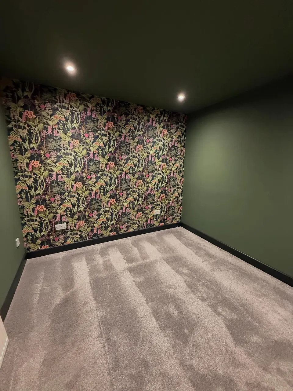 Floral wallpaper feature wall in a dark green painted room
